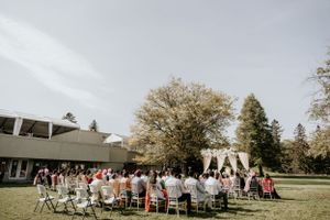 Guests seated in white chairs for an outdoor wedding ceremony with blooming trees in the background.