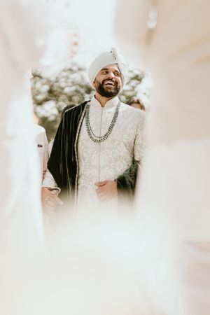 Wedding guest in traditional white sherwani with black jacket and ornate necklace.
