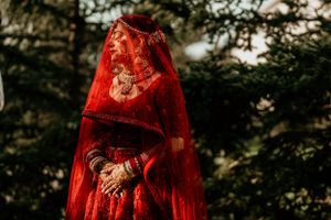 Traditional red wedding attire with intricate embroidery and veil detail against a natural outdoor backdrop.
