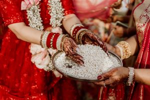 Close-up of hands with mehndi designs holding rice during traditional Indian wedding ritual.