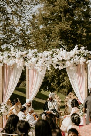 Outdoor Indian wedding ceremony under pink and white floral mandap with flowing drapes.
