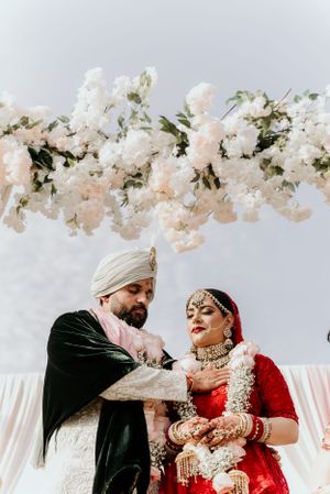 Traditional Indian wedding couple under a canopy of delicate white and blush floral arrangements.