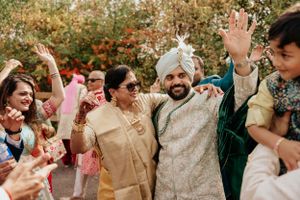 Joyous wedding celebration with guests dancing in traditional Indian attire outdoors.