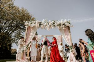 Celebratory moment during outdoor wedding ceremony under pink and white floral mandap.