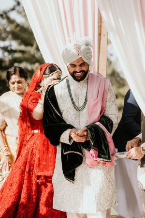 A joyful moment during a traditional Indian wedding ceremony under a decorated mandap with pink and white drapes.
