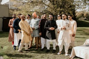 Group photo of wedding guests in traditional formal attire gathered on sunny lawn.