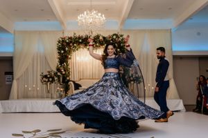 Dancing figure in a flowing navy gown twirls on the dance floor under crystal chandeliers.