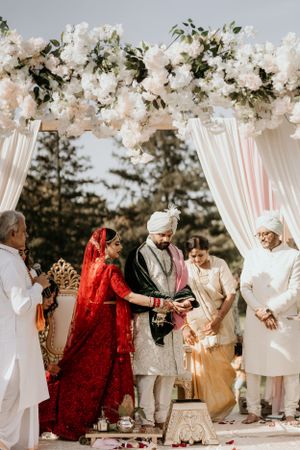 Traditional Indian wedding ceremony taking place under an elegant floral arch with white draping and flowers.