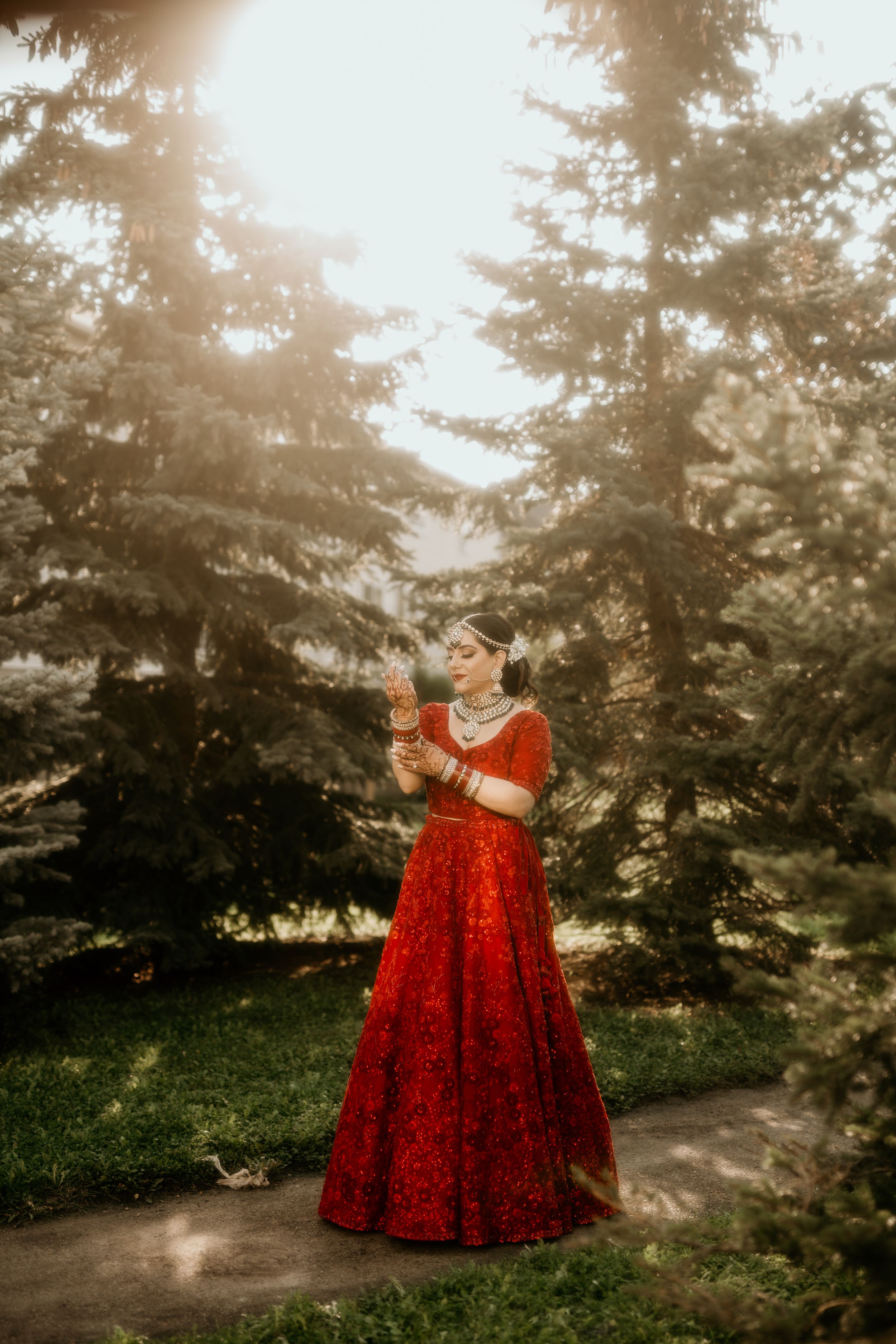 Dreamy outdoor portrait of bride in red gown surrounded by towering evergreen trees.