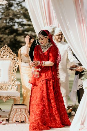 Wedding celebration with person in vibrant red lehenga under decorated mandap.