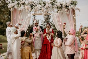 Wedding guests celebrating during an Indian ceremony under floral mandap with pink and white draping.