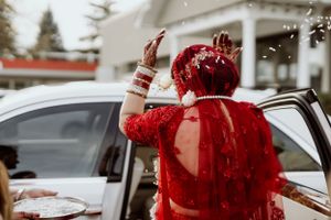 Person in red traditional Indian wedding attire throwing rice during celebration ritual.