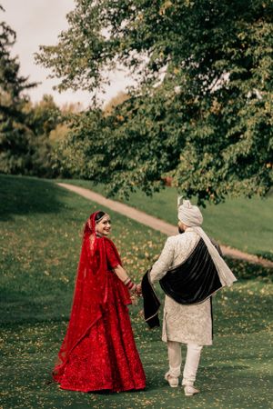 Couple in traditional wedding attire walking along a scenic garden path.