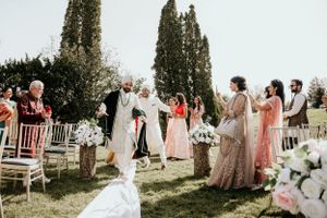 Outdoor wedding ceremony with white chairs and floral decorations in garden setting.