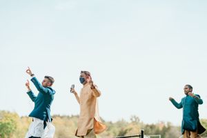 Three people jumping joyfully outdoors in traditional Indian attire.