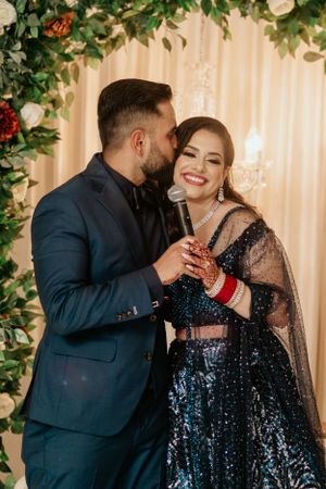 Glamorous couple sharing joyful moment under floral arch at wedding reception.