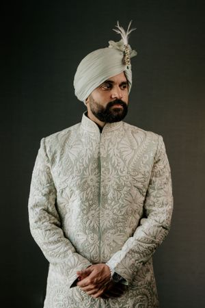 Elegant white embroidered sherwani and turban with brooch shown in formal portrait style.