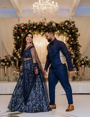Couple in navy formal wear pose beneath an elegant floral arch with chandelier.