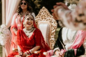 Traditional Indian bride in red attire seated on an ornate golden throne during wedding celebrations.