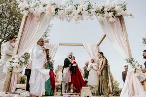 Traditional Indian wedding ceremony under an elegant floral mandap with blush pink drapes and white flowers.