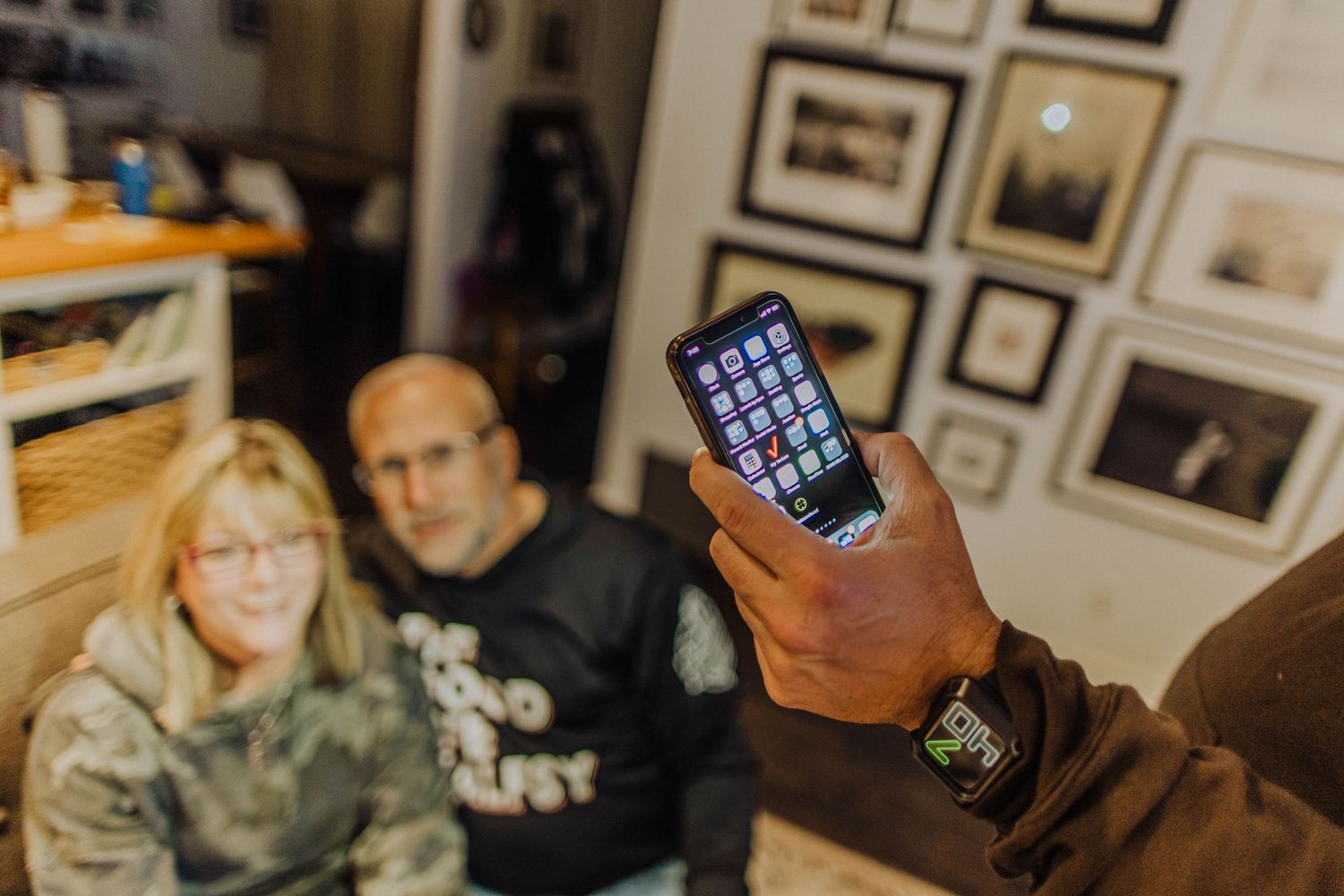 Group gathered in a living room with framed photographs examining their phones.