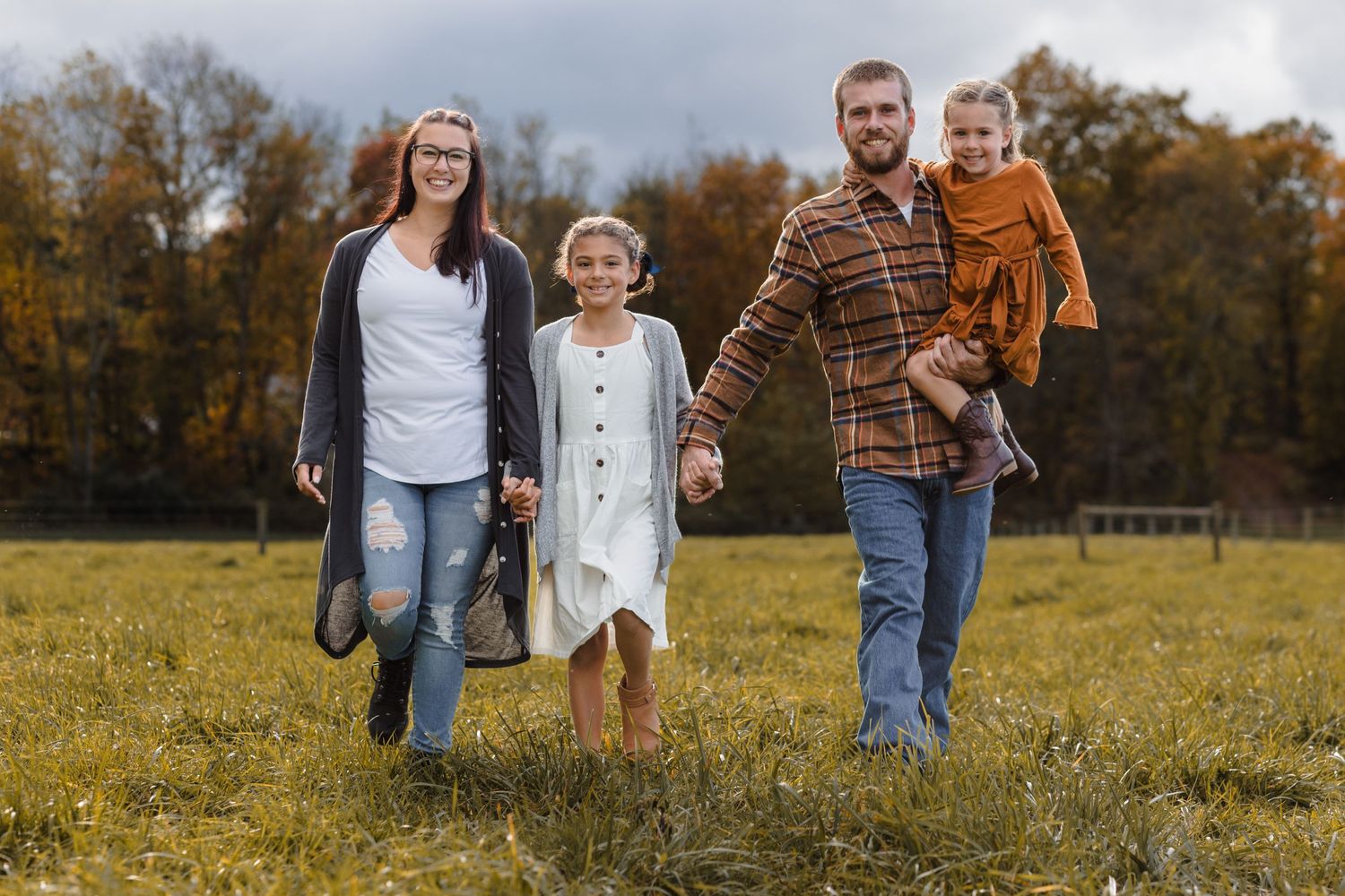 Family walks together through sunny autumn field during outdoor photoshoot.