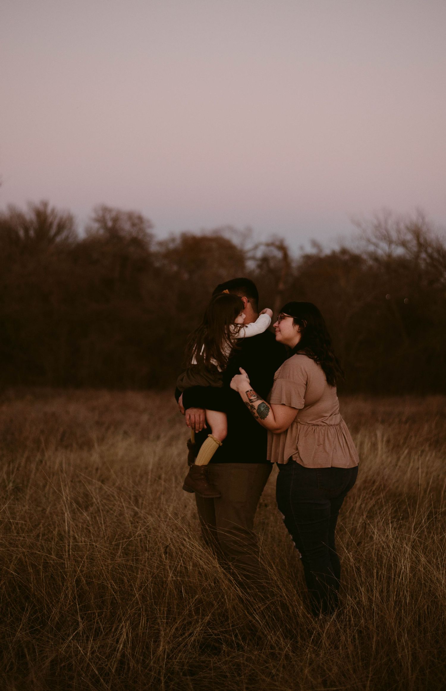 Family sharing joyful moment together in tall grass field during sunset.