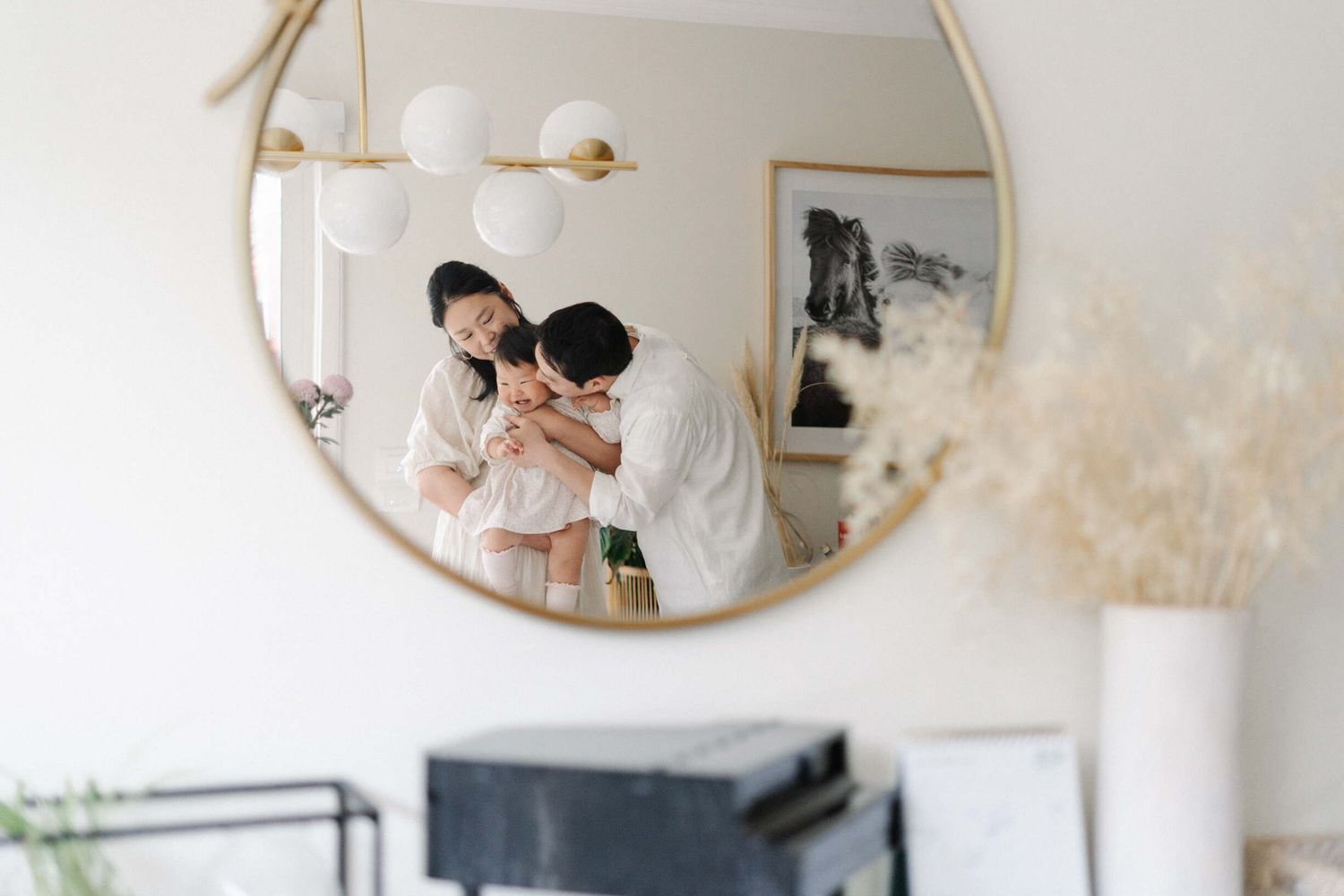 A two-year-old being held by mom and dad smiling, captured in the reflection of a mirror in their home in Melbourne.