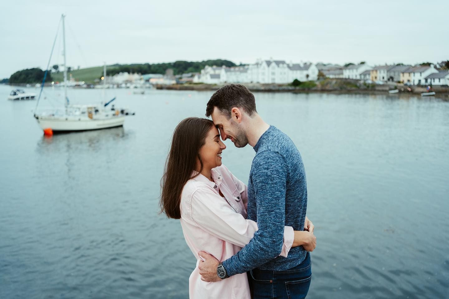 A romantic seaside photoshoot with a couple embracing against a coastal backdrop.