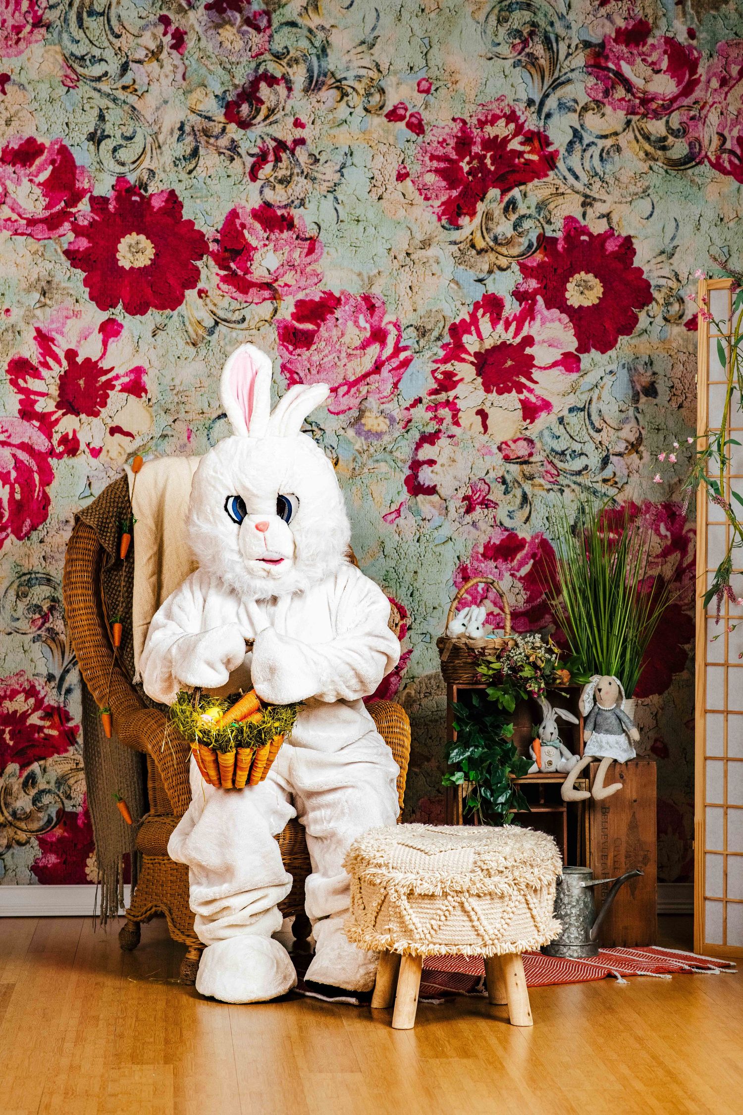 Easter bunny costume sitting in peacock chair against floral wallpaper backdrop.