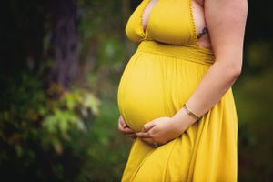 Close up of pregnant belly in flowing yellow maternity dress outdoors.