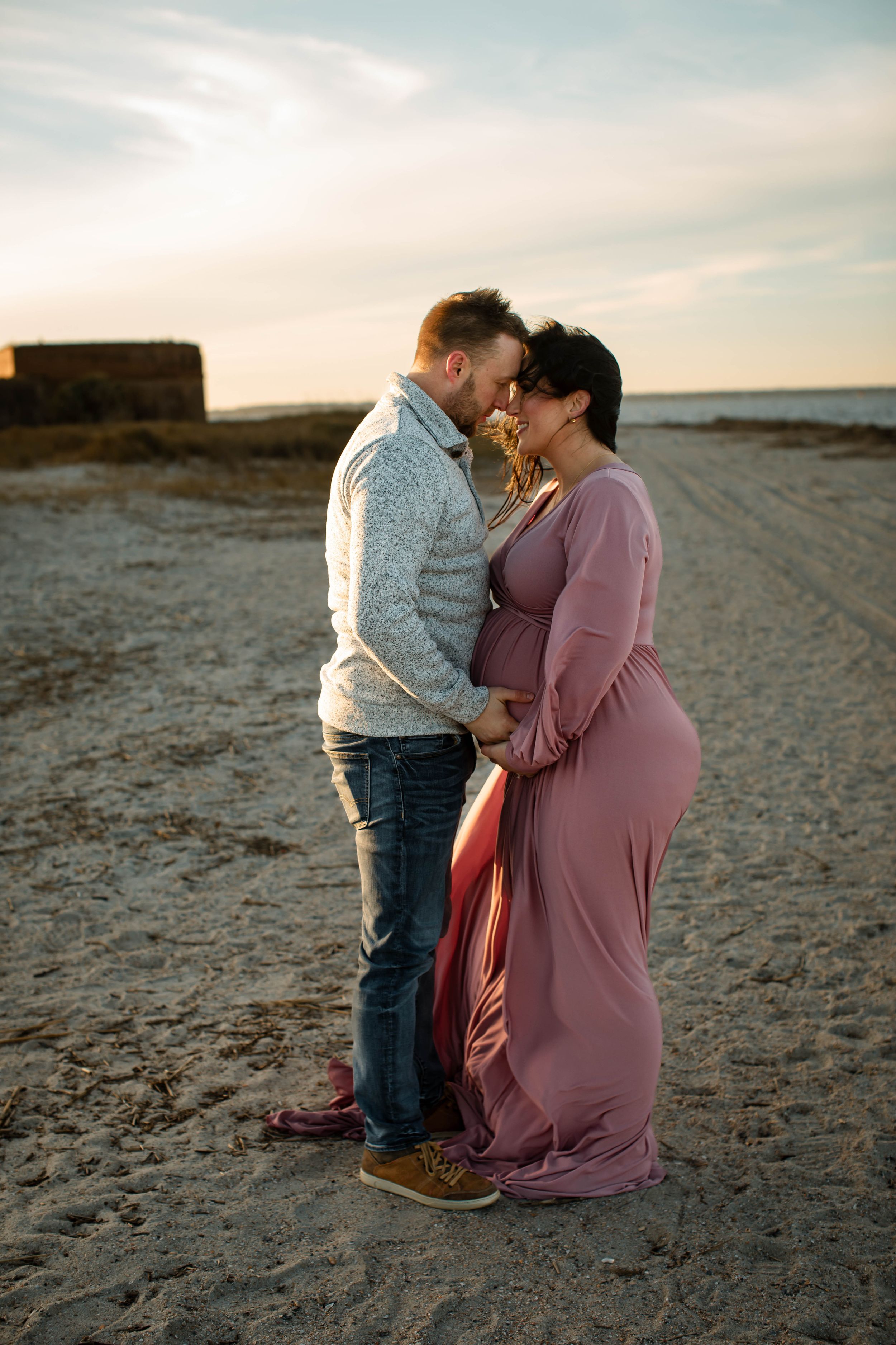 A romantic sunset maternity photo session on a beach with warm golden light.