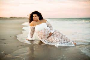 Person in white lace dress laying on beach at sunset with ocean waves in background.