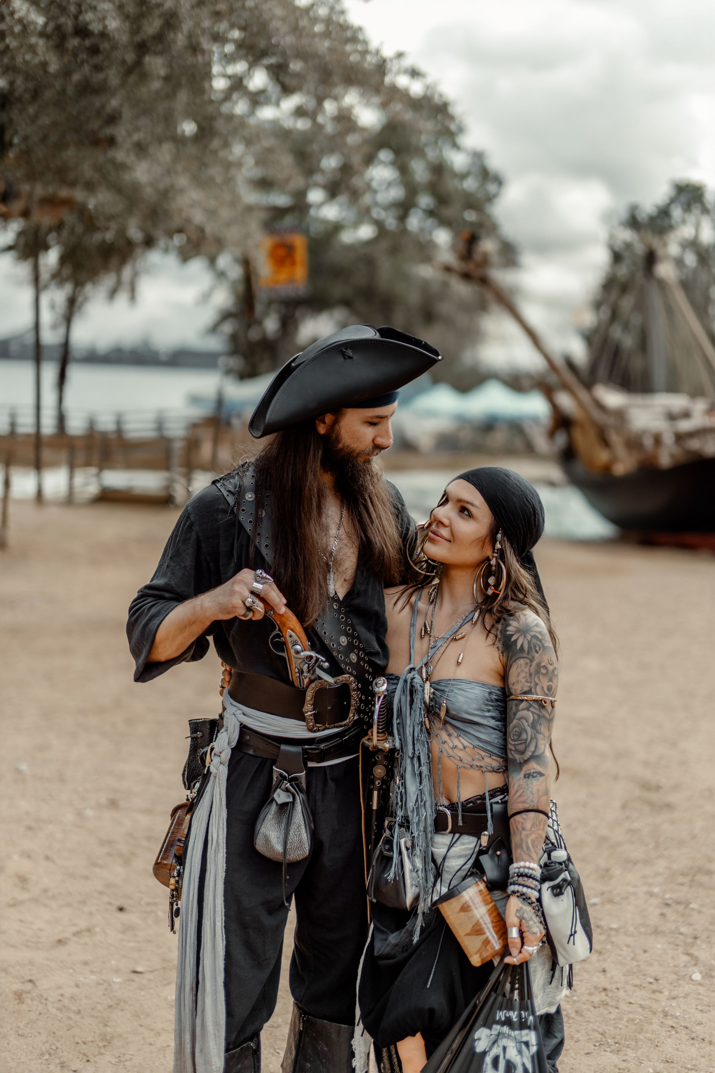 Pirate-themed couple portrait on beach with period costumes and props.
