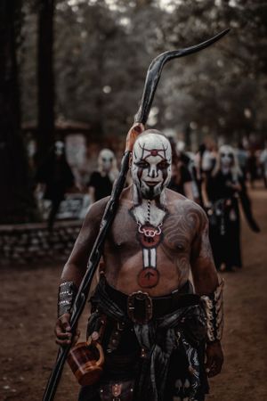 A painted warrior with tribal markings holds a staff at a renaissance fair.