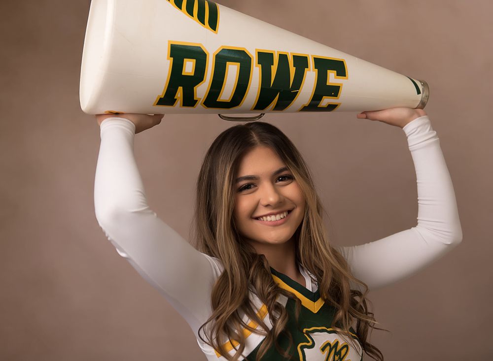 Cheerleader holds white and green Rowe megaphone overhead in celebration pose.