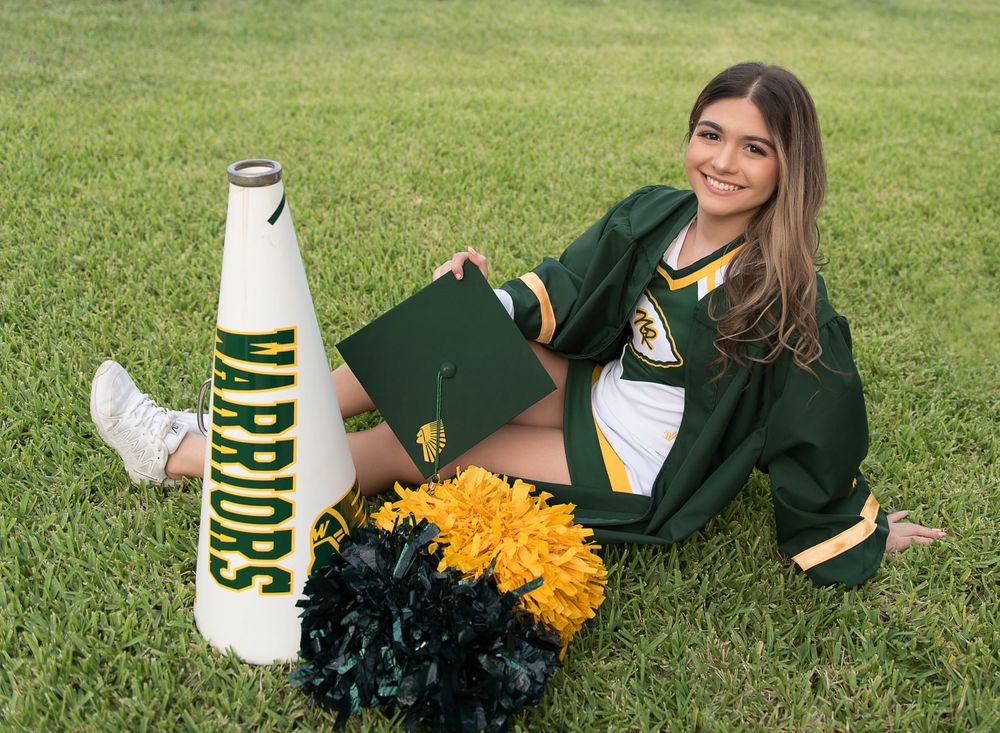 Cheerleader poses with pom poms and megaphone on grass field in school colors.