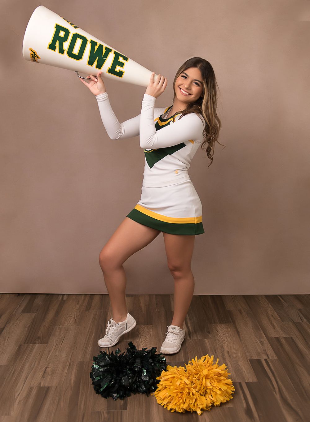 Cheerleader poses with Rowe megaphone and pom poms on hardwood floor in studio setting.