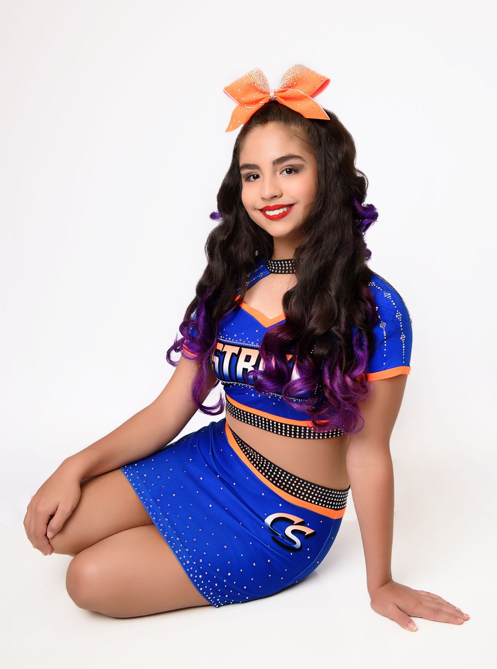 Cheerleader wearing blue uniform with orange bow poses in studio setting.