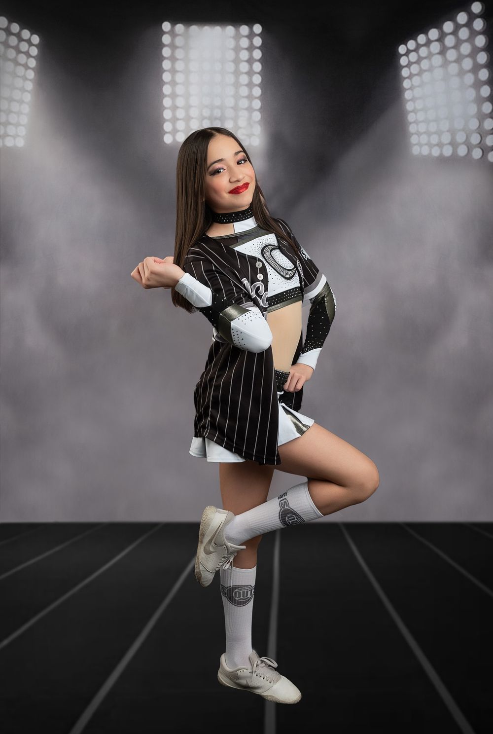 Cheerleader performing in black and white uniform under stadium lights.