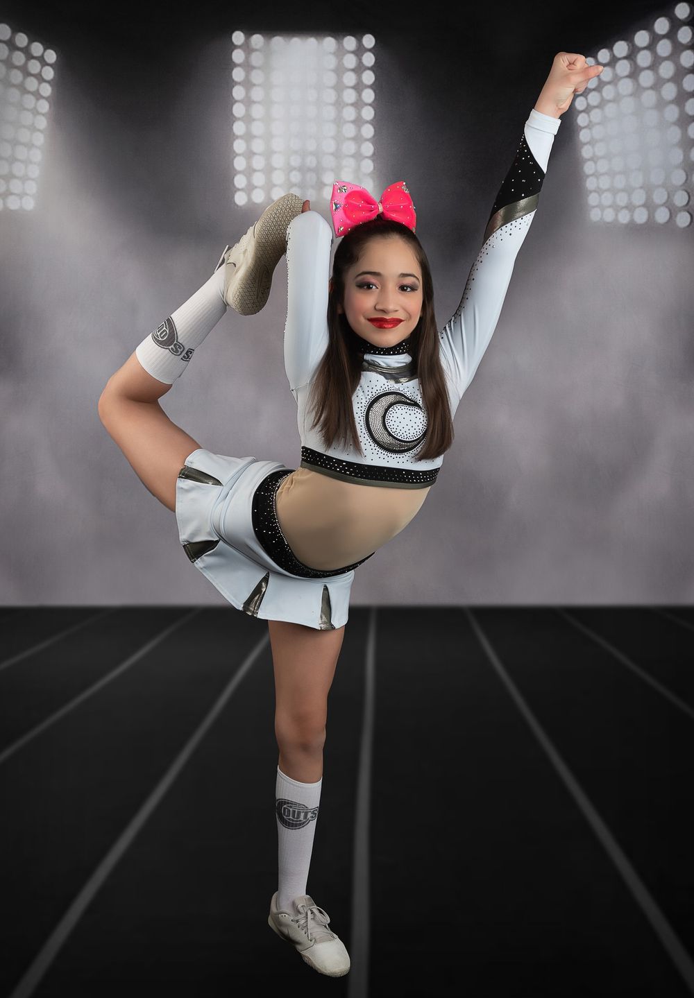 Cheerleader performing flexible leg hold pose in white uniform.