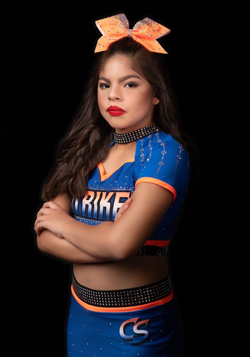 Cheerleader poses in blue and orange uniform with matching bow.