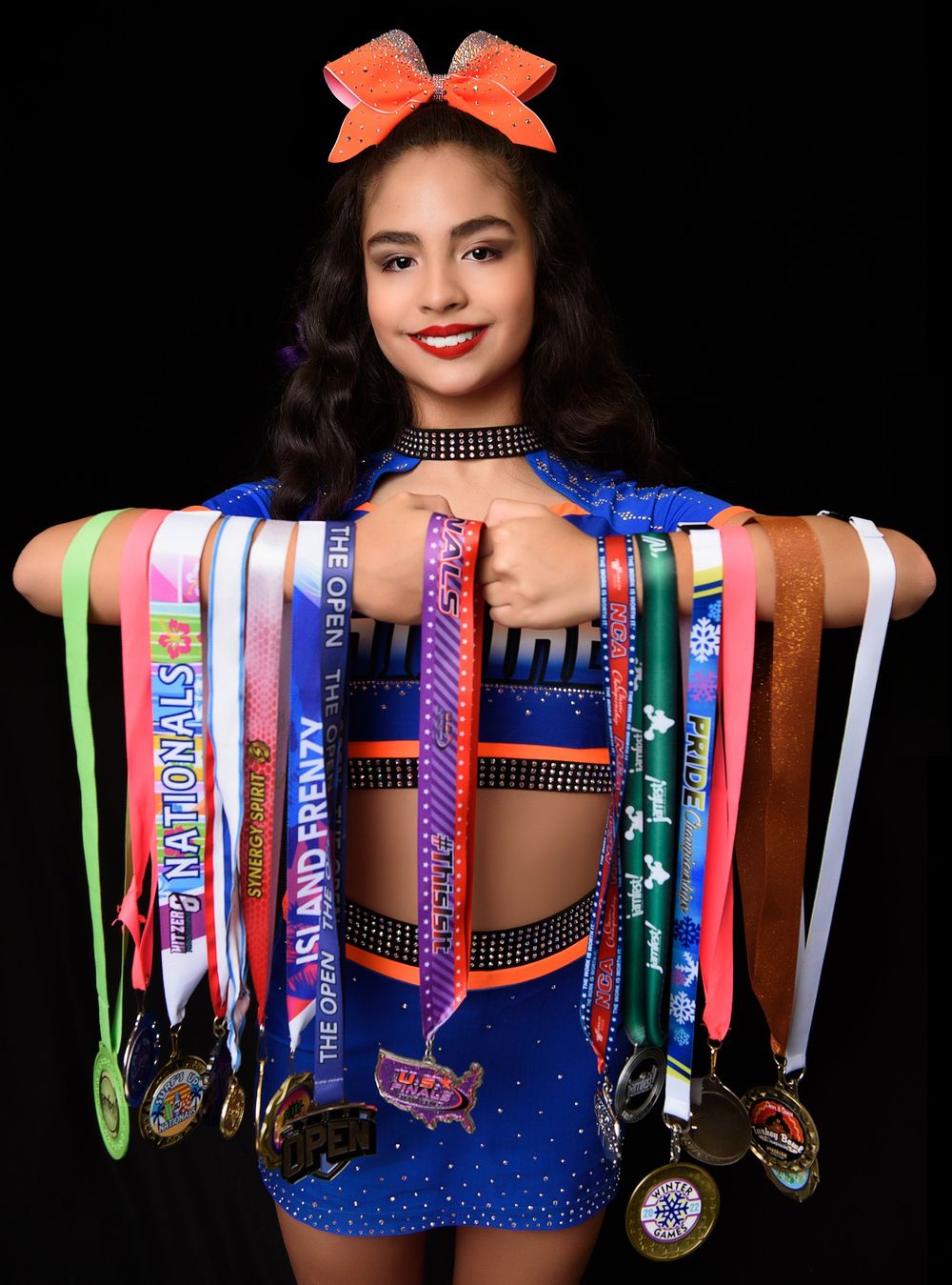 A cheerleader displays collection of competition medals while wearing blue sparkly uniform.