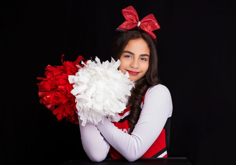 A cheerleader holds red and white pom poms while wearing a traditional uniform.