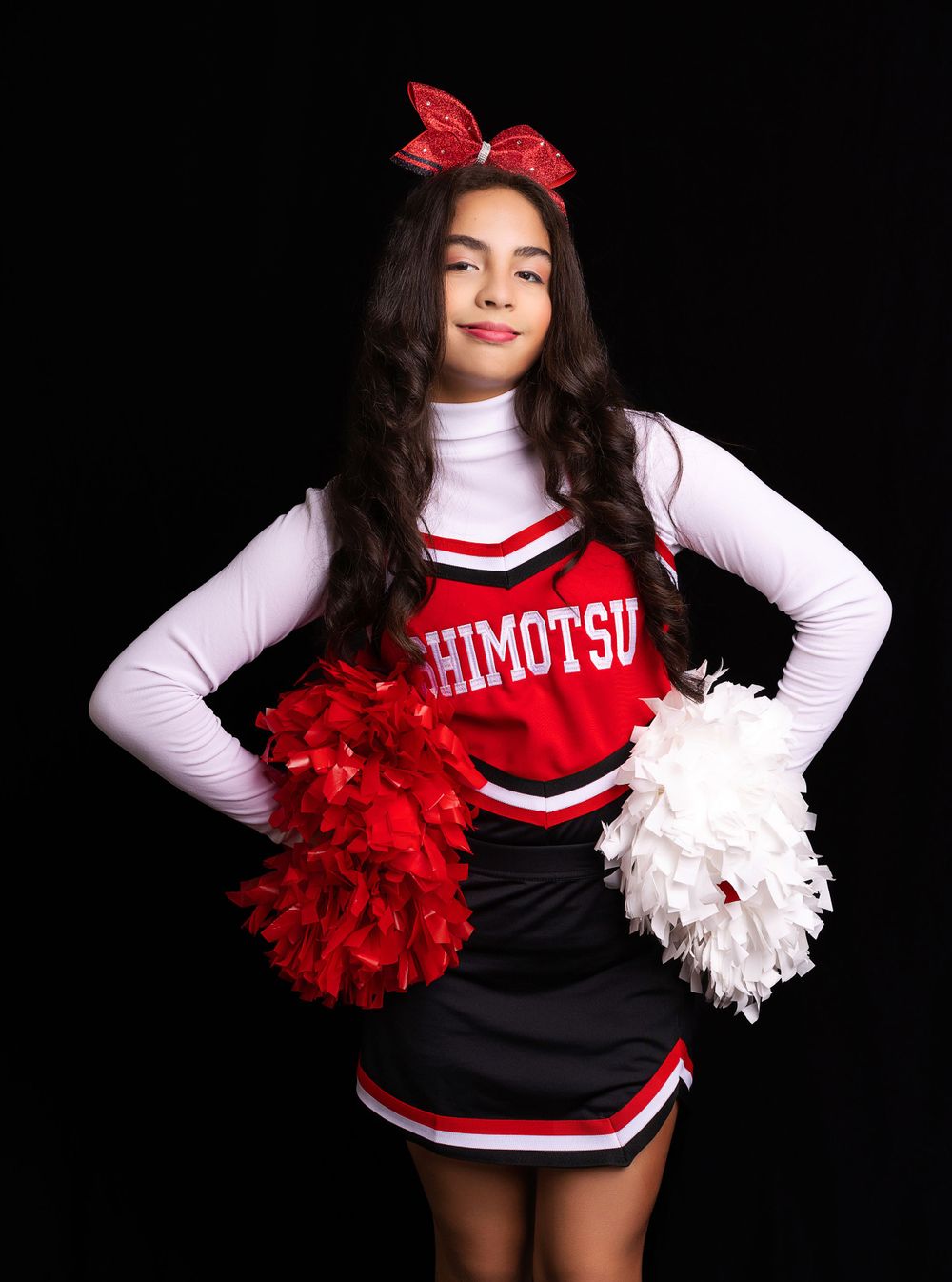 Cheerleader poses with red and white pom poms wearing Shimotsu uniform and red bow.
