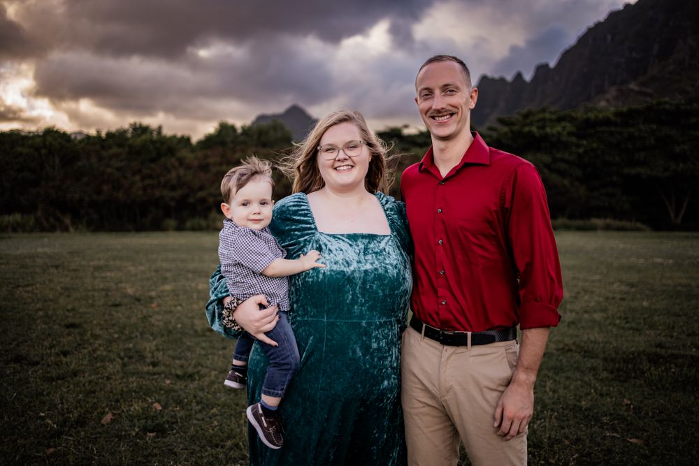 A family portrait taken outdoors with dramatic mountain peaks and moody clouds in the background.