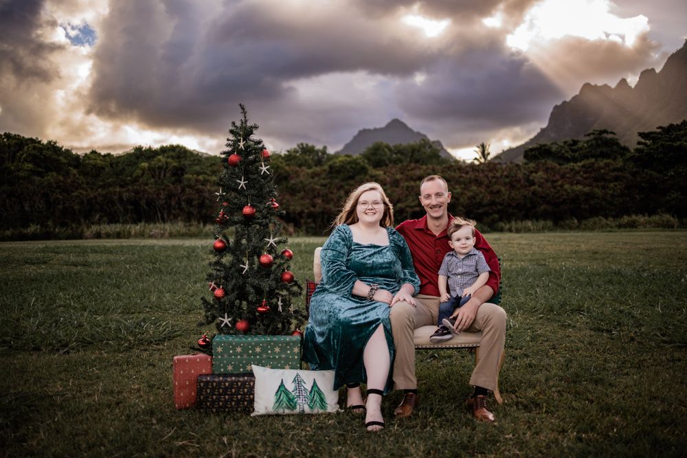 A holiday family photo with Christmas tree and wrapped presents in a scenic mountain setting.