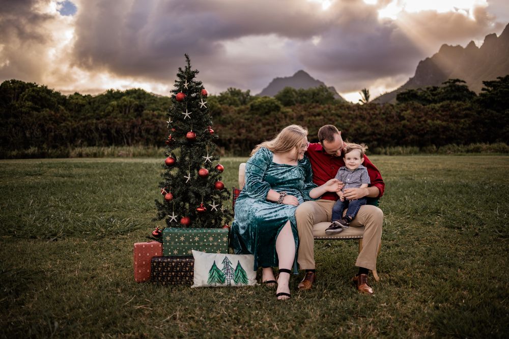A family shares a tender moment on a bench beside a decorated Christmas tree outdoors.