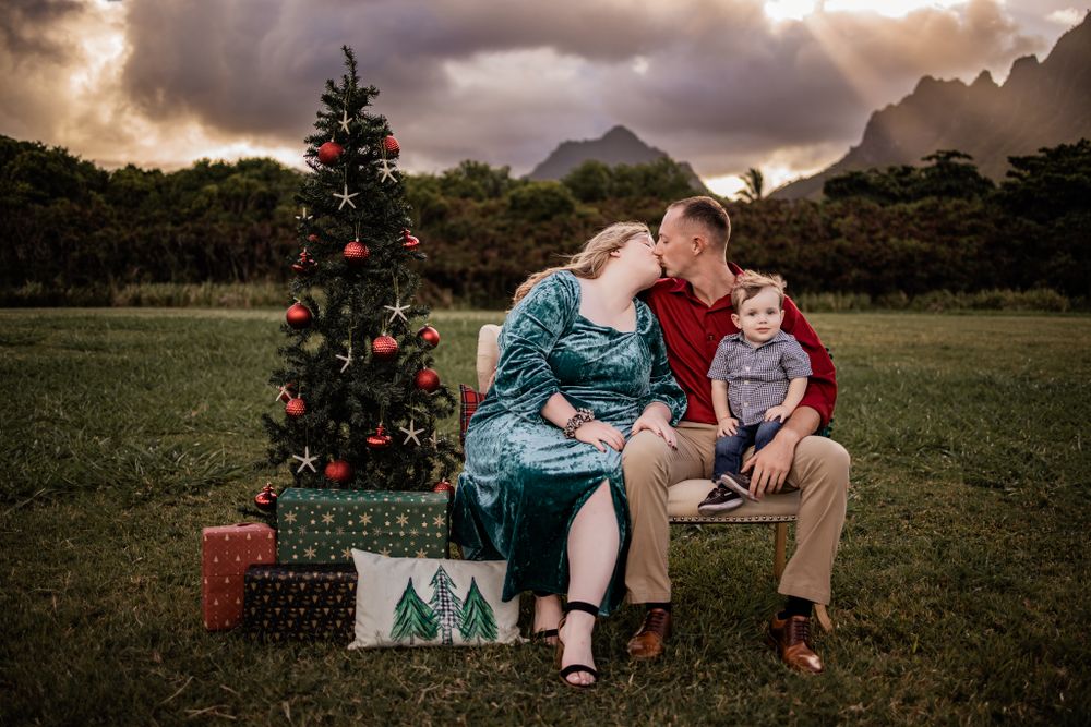 A family sits together on a bench by a decorated Christmas tree with mountains in the background.