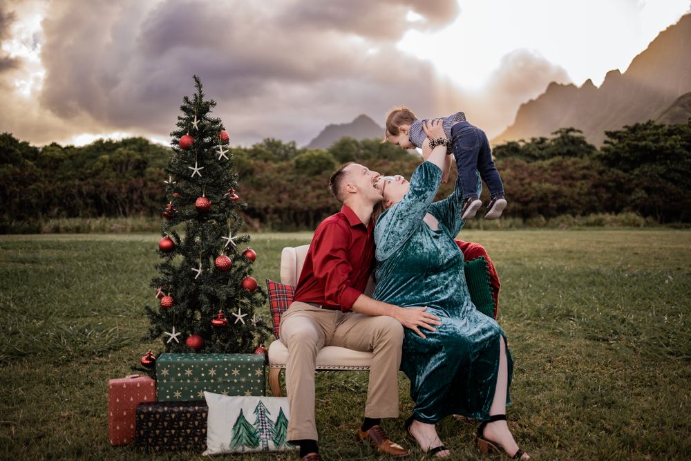A playful family moment captured near a Christmas tree with mountains and dramatic sky.